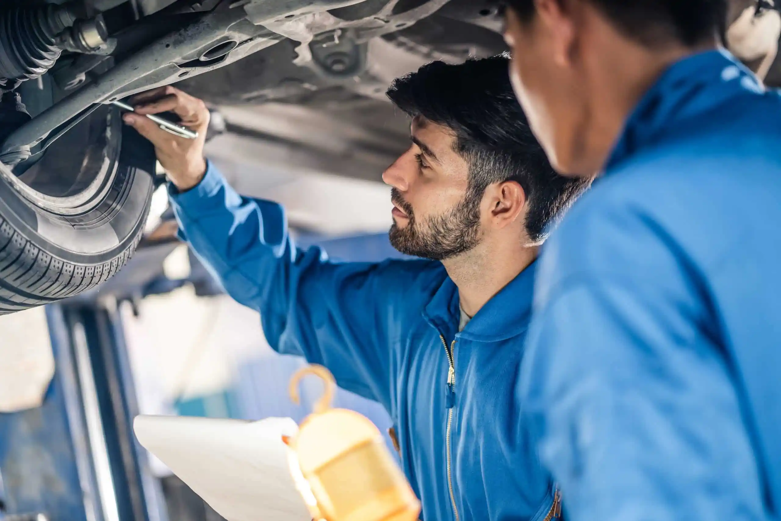 mechanics checking wheel of vehicle suspended on hydraulic lift